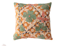 Suzani pillowcase in boho vintage style with orange base and white floral ornaments as well as large green leaves with pink dots and dark blue winding tendrils.